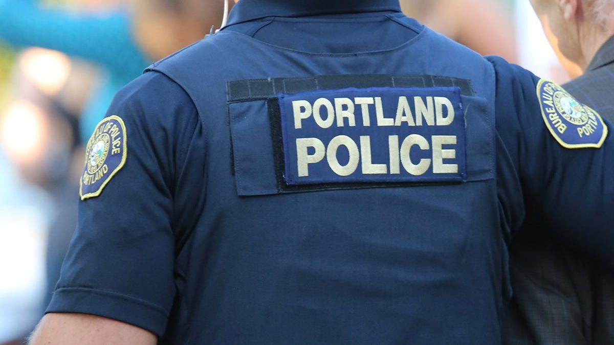 La photo montre un policier portant un gilet indiquant « Portland Police »